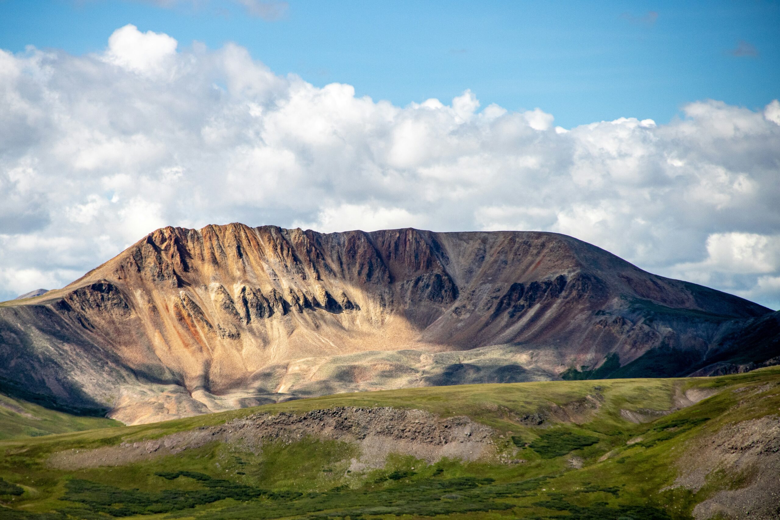 Dramatic, snow-dusted peaks of the San Juan Mountains rising above an alpine meadow during golden hour.