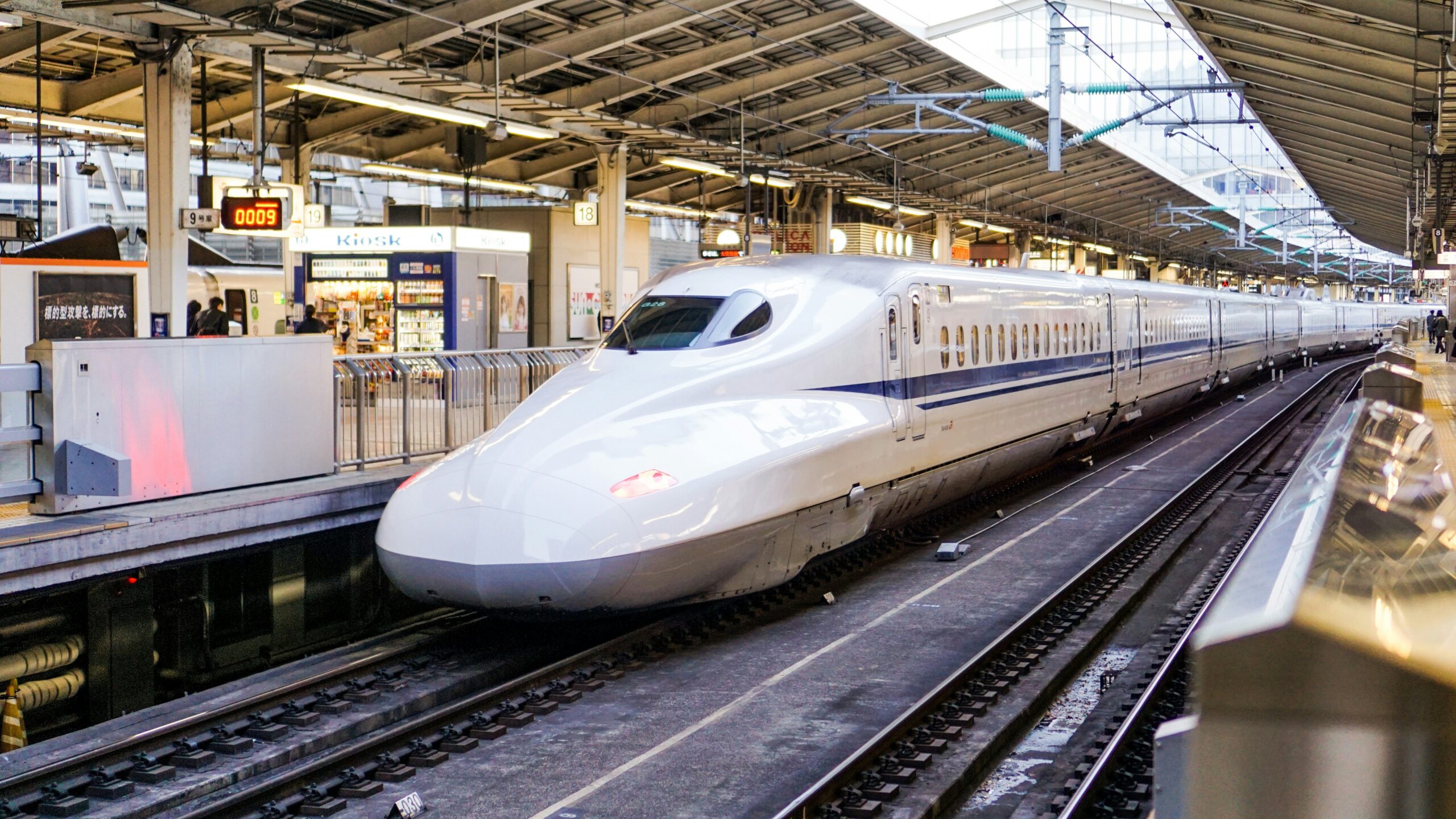 Sleek white nose of a Shinkansen bullet train parked at Tokyo Station platform with passengers waiting to board.